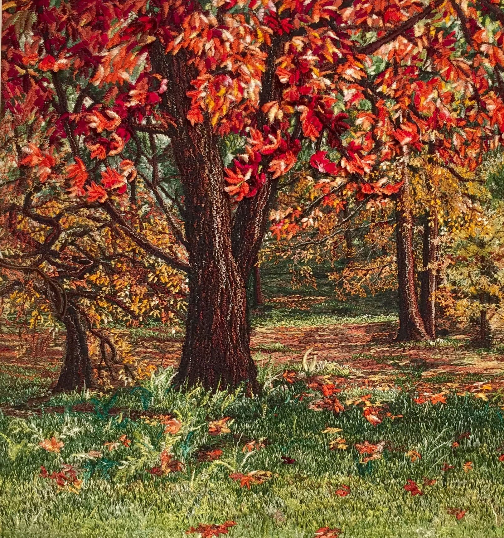 Autumn trees with red and orange leaves over a green woodland floor, stitched in thread