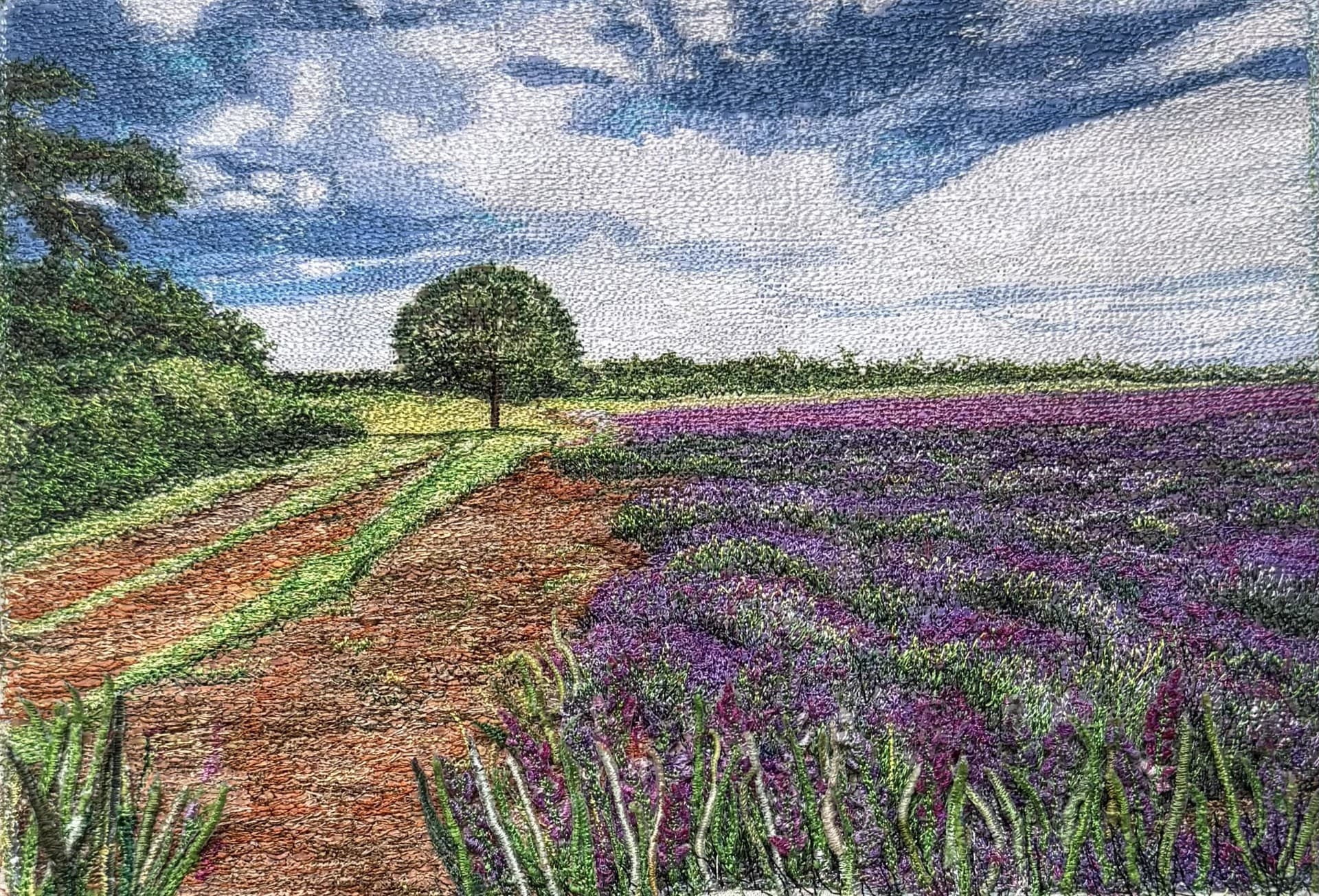 A track beside a field of lavender, with a single tree under a cloudy sky