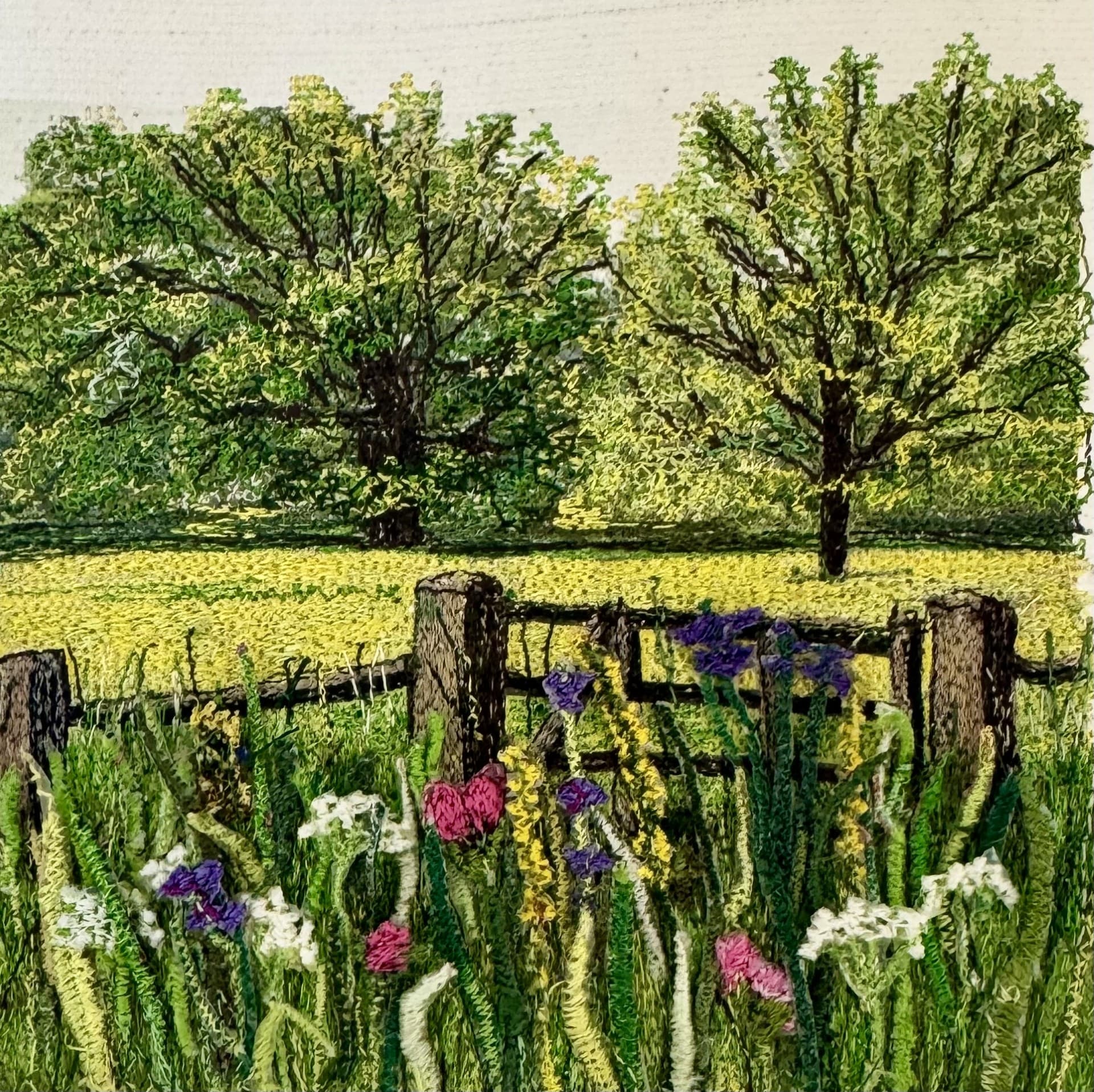 A yellow field behind a wooden fence, with trees and flowers in the foreground